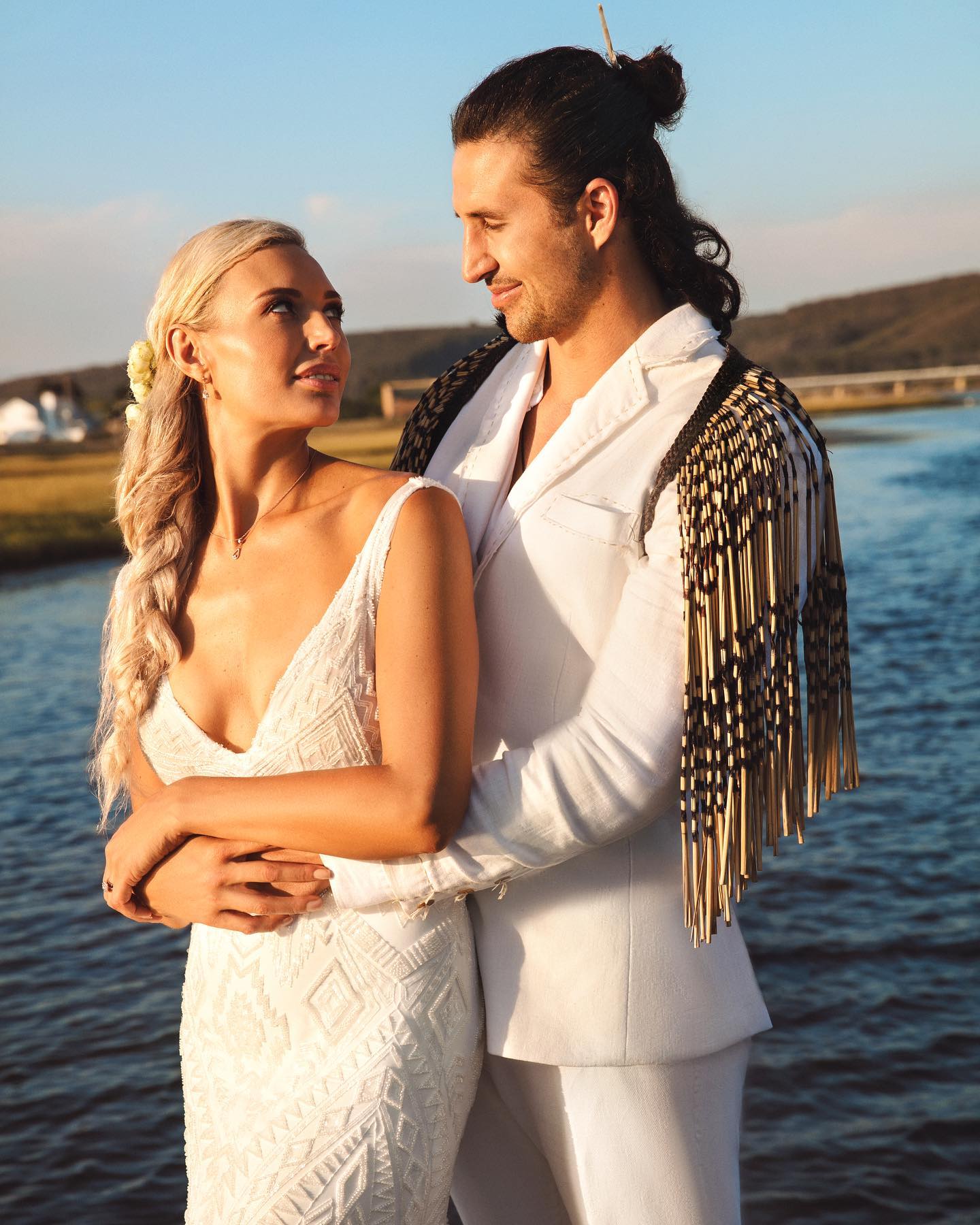 Sam Barton and Roxy Louw in their wedding outfits beside the water.