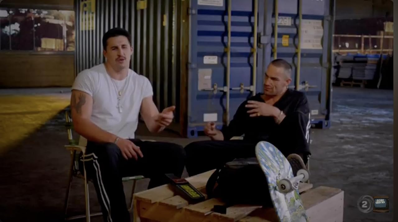 Sam Barton rapping as Gangster Rapper in Terry Teo, seated in a white T-shirt beside another character in A Penny for Your Troubles.
